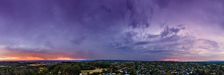 Stormy rain clouds in the afterglow of sunset glowing purple, blue and orange aerial panoramic