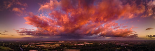 Firey storm clouds orange pink and red at sunset with distant rain storm across the landscape aerial panoramic