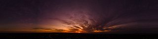 Dark wispy clouds in a deep purple sky at the end of a glowing orange sunset aerial panoramic
