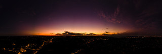 Dark horizon clouds in a deep purple sky in the afterglow of an golden sunset above the street lights aerial panoramic