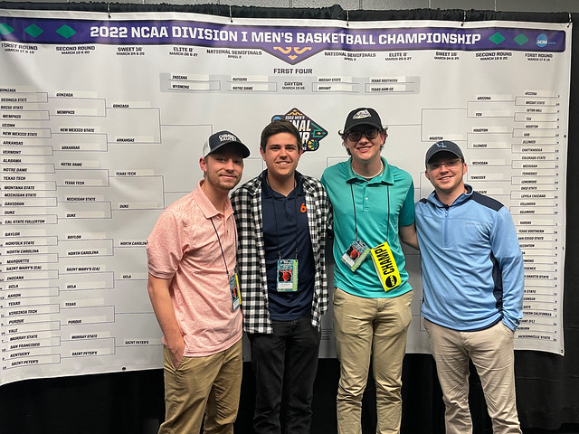A group of students stand in front of a March Madness bracket.