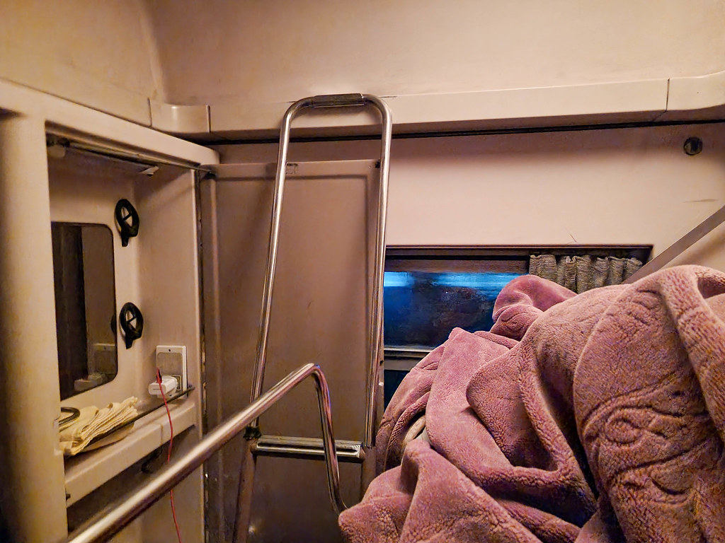 A photo taken from the top bunk bed in the cabin. On the right hand side there is a brown blanket. On the left you can see the ladder to climb up, next to a mirror.