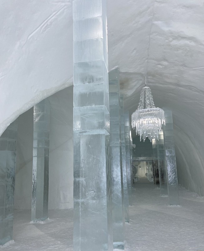 Carved out ice tunnel with rectangular ice pillars and an ice chandelier hanging in the back.