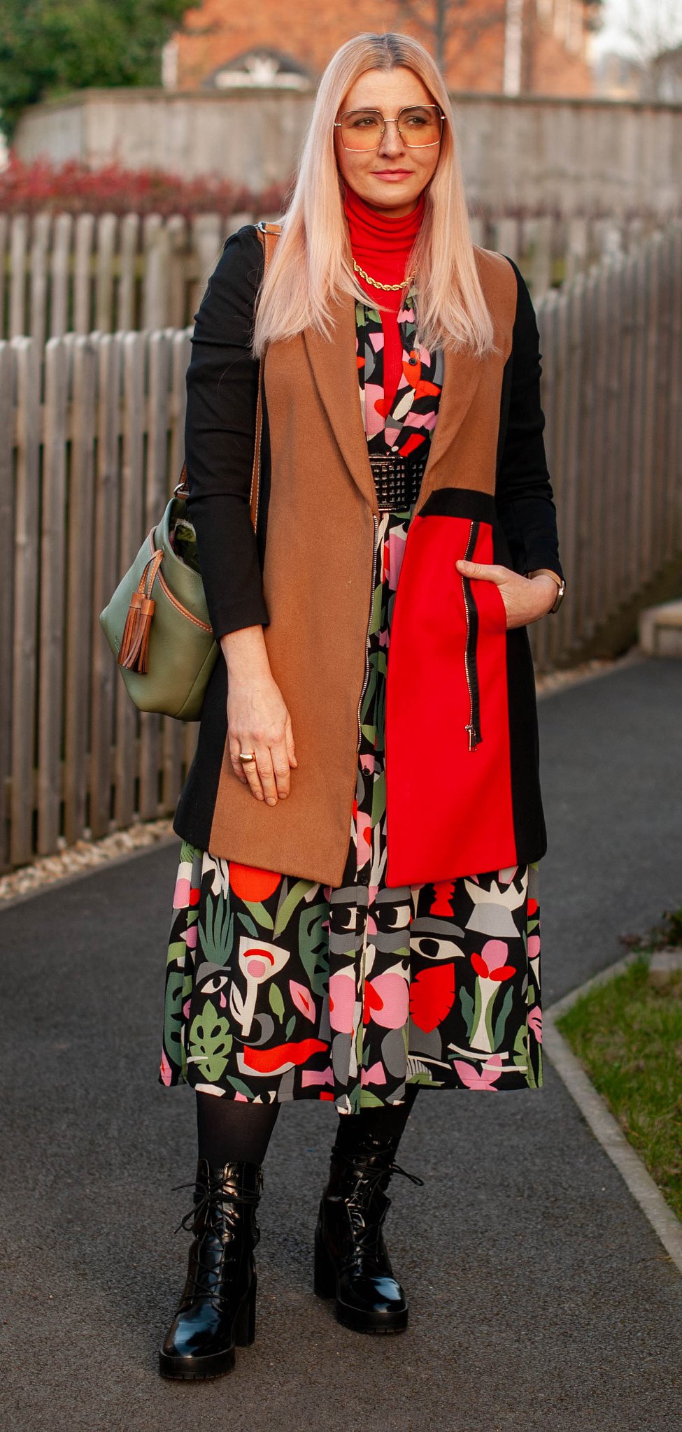 A Touch of 1970s Styling With Rich Colour and Bold Print: Catherine Summers AKA Not Dressed As Lamb wearing a dark tropical print midi dress, black lace-up boots, red roll neck, gold chunky jewellery and a black, red and camel colour block coat | Over 40 Style