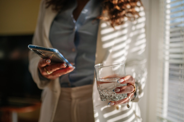 Woman in a business suit holding a smartphone and a glass of water