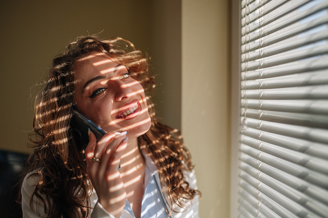 Young woman talking on the phone call while while standing next to an office window