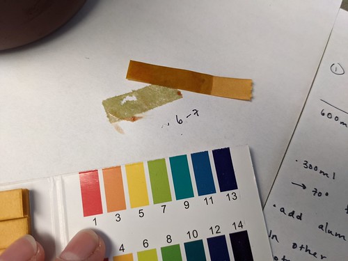 Used pH strip lying next to pH color chart and strip color mark, color mark is greenish and labeled 6-7