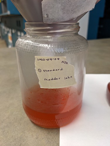 Reddish liquid drained through filter into Standard Madder Lake jar, now more full