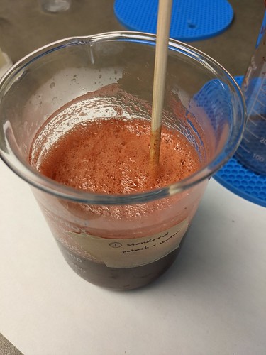 Overhead shot of Standard Potash and Water beaker, which is full of reddish liquid and pinkish foam