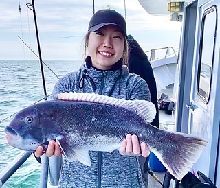 Photo of a woman on a boat on the ocean, holding a tautog