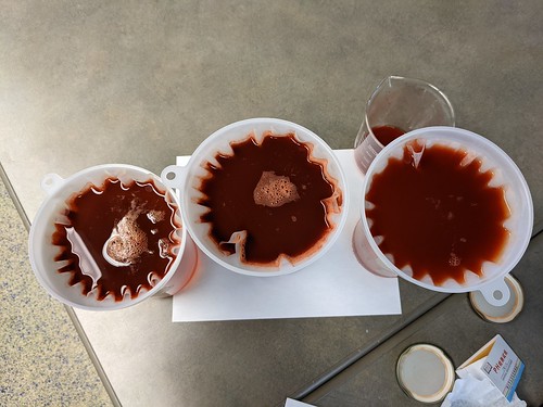 Overhear shot of three jars with funnels and filters, each draining reddish liquid into the jar below
