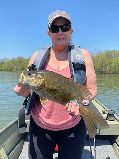 Photo of a woman on a small boat in a river, holding a smallmouth bass