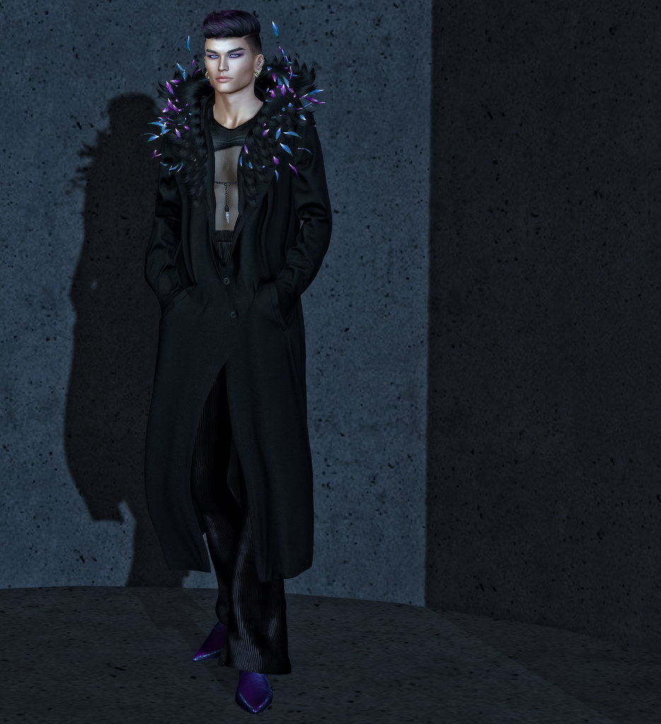A black-haired man standing in front of a wall that appears lit by moonlight. He's wearing a long black coat, buttoned loosely at his waist. The lapels and collar of the coat comprise a black feather boa with swirling aqua and purple pieces coming out of it, that is held together by a short black chain with a crystal pendant hanging from it. His pants are loose black corduroy and his boots are iridescent purple-teal winklepickers. In his hair you can just make out faint streaks of purple that match the shoes.