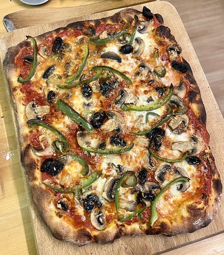 A photo of a roughly rectangular pizza, taken from above, with peppers, mushrooms and olives visible on the cheese and tomato that sits on a crispy-looking base