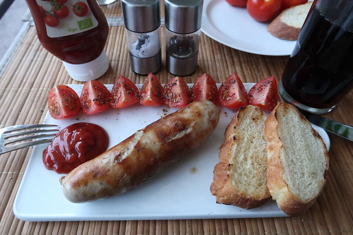 Gegrillte Bratwurst mit Ketchup, angerösteten Baguettescheiben und aufgeschnittenen Tomaten