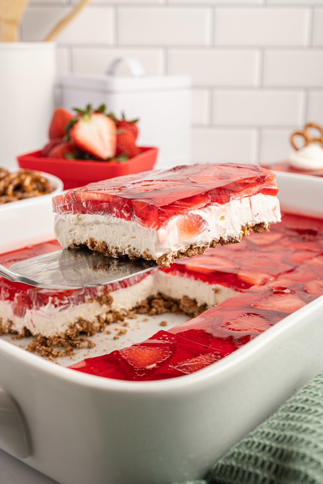 A slice of strawberry pretzel salad on a spatula with the rest of the pan in the background