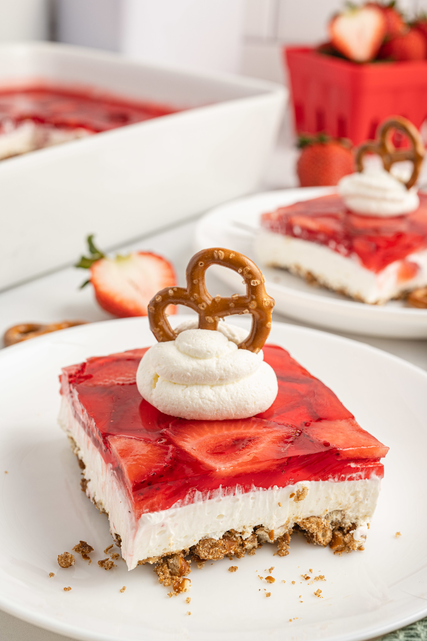 A slice of strawberry pretzel salad with whipped cream and a pretzel on top