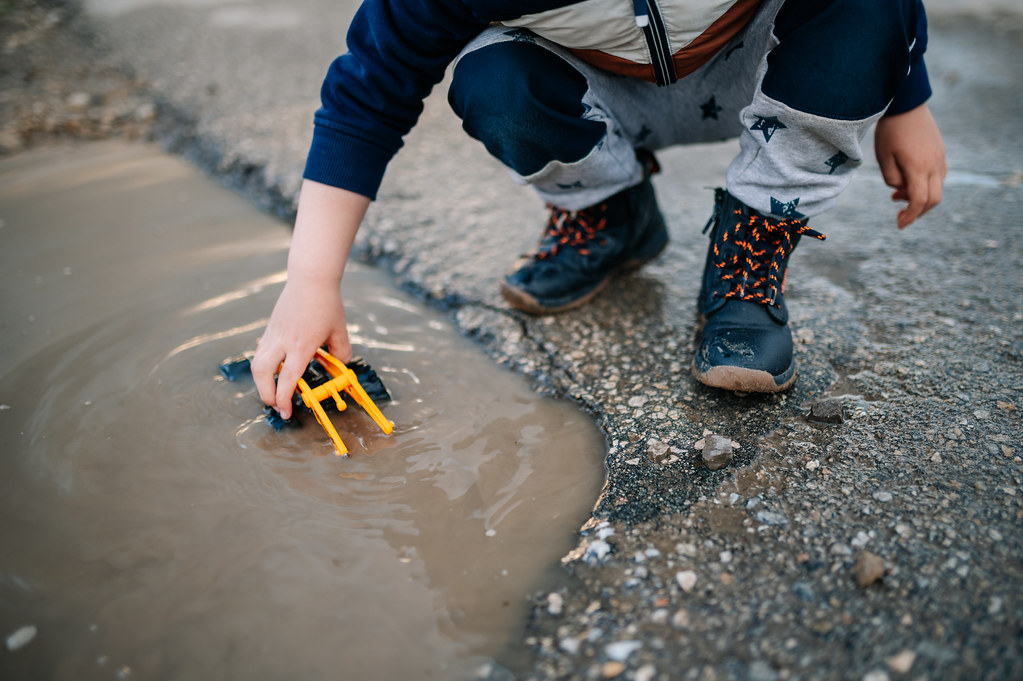 Boy playing with his toy vehicle by soaking it in a puddle