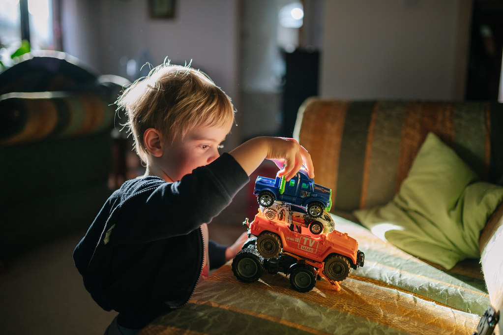 Young boy playing by stacking his toy vehicles on the couch
