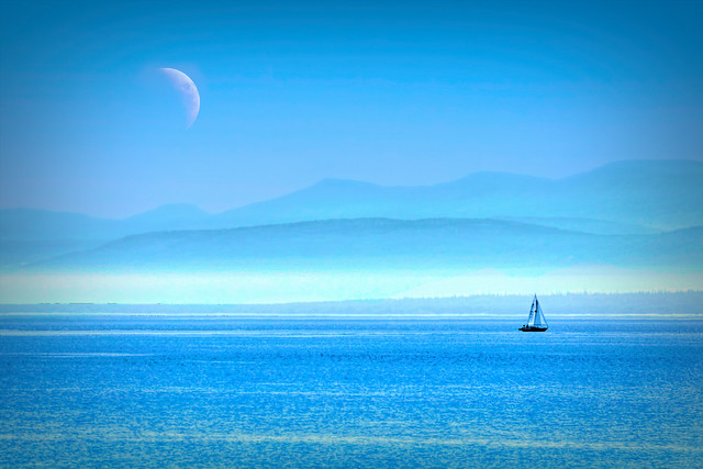 Sea, Mountains and Moon Dwarfing a Sailboat