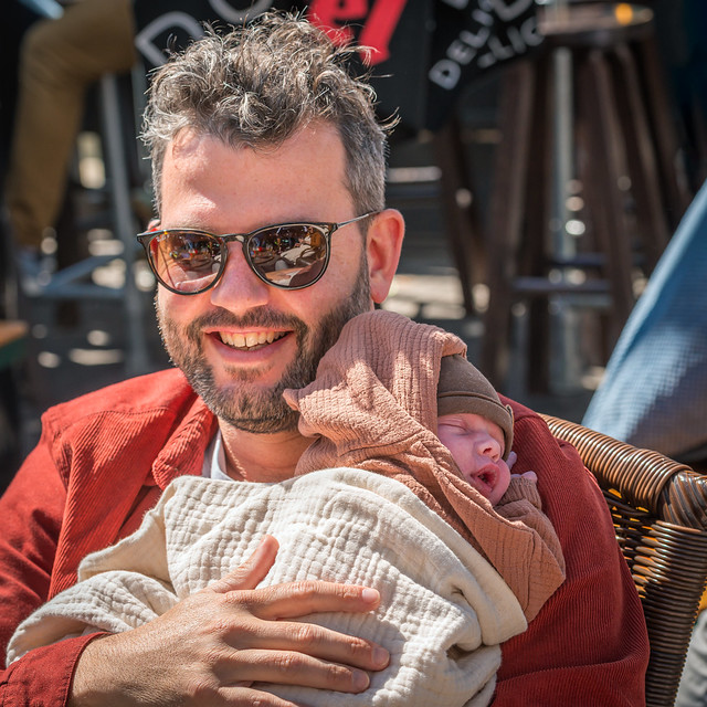 Portrait of a proud father sitting on a terrace with his newborn baby