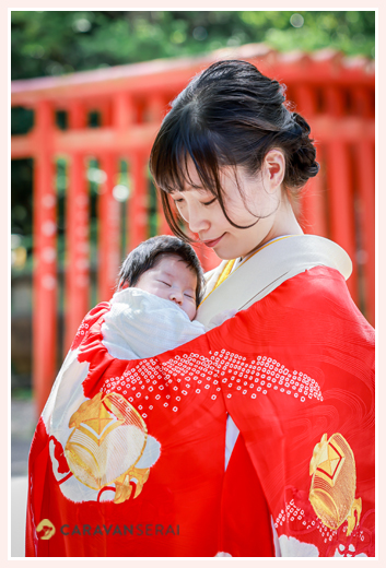 お宮参り　赤の産着にくるまれた赤ちゃんを抱っこするママ