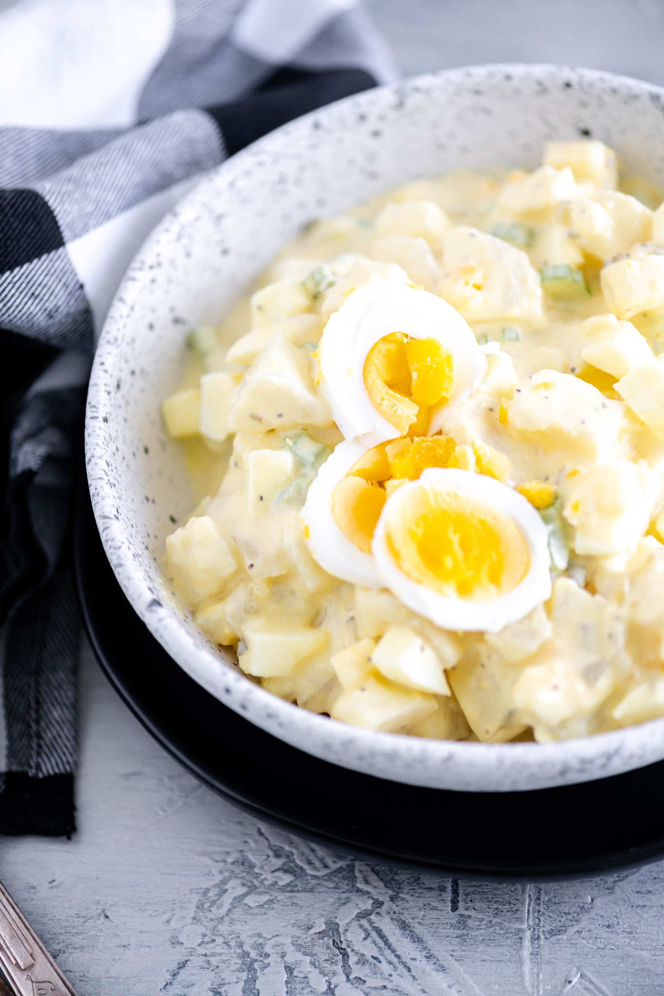 Potato salad in a white bowl with black speckles.