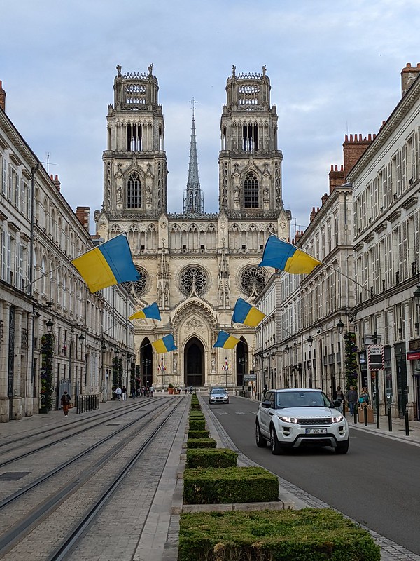 View of Orleans cathedral, looking down a boulevard from a distance, with rows of houses and Ukrainian flags to either side