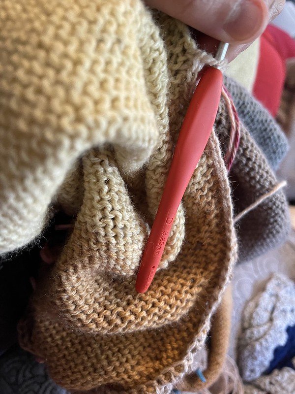 close up on a D / 3.25mm crochet hook being used to assemble a machine knit sweater with single crochet