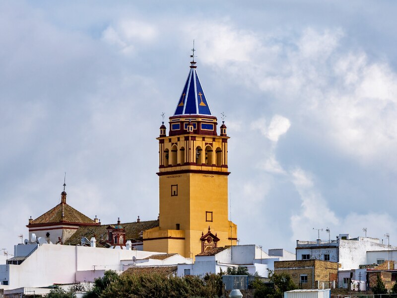 The yellow tower of the church in El Coronil. The rooftop of the church is blue