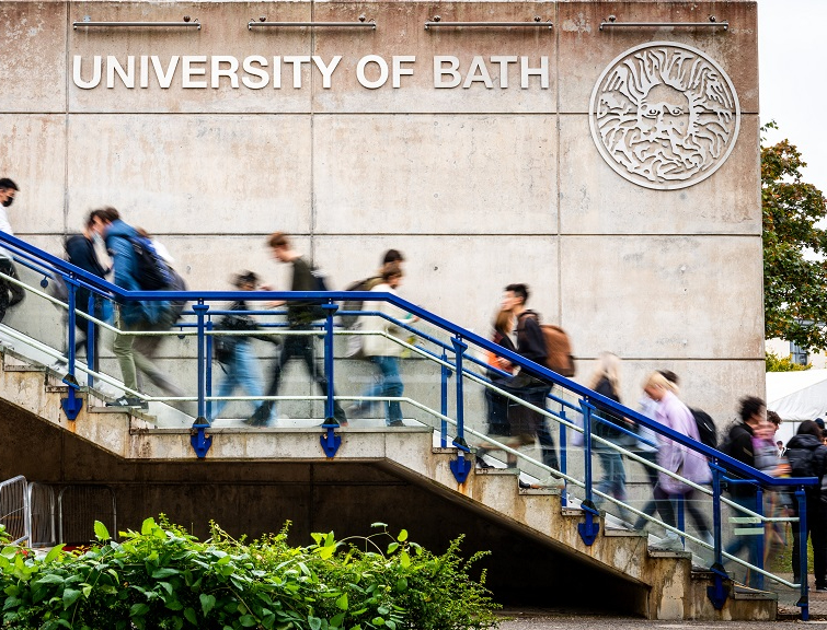 Students walking up an outside staircase past a University of Bath sign.