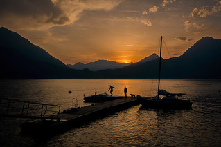 Silhouette of two men and a dog on the dock just as the sun sets over Lake Como in Varenna, Italy