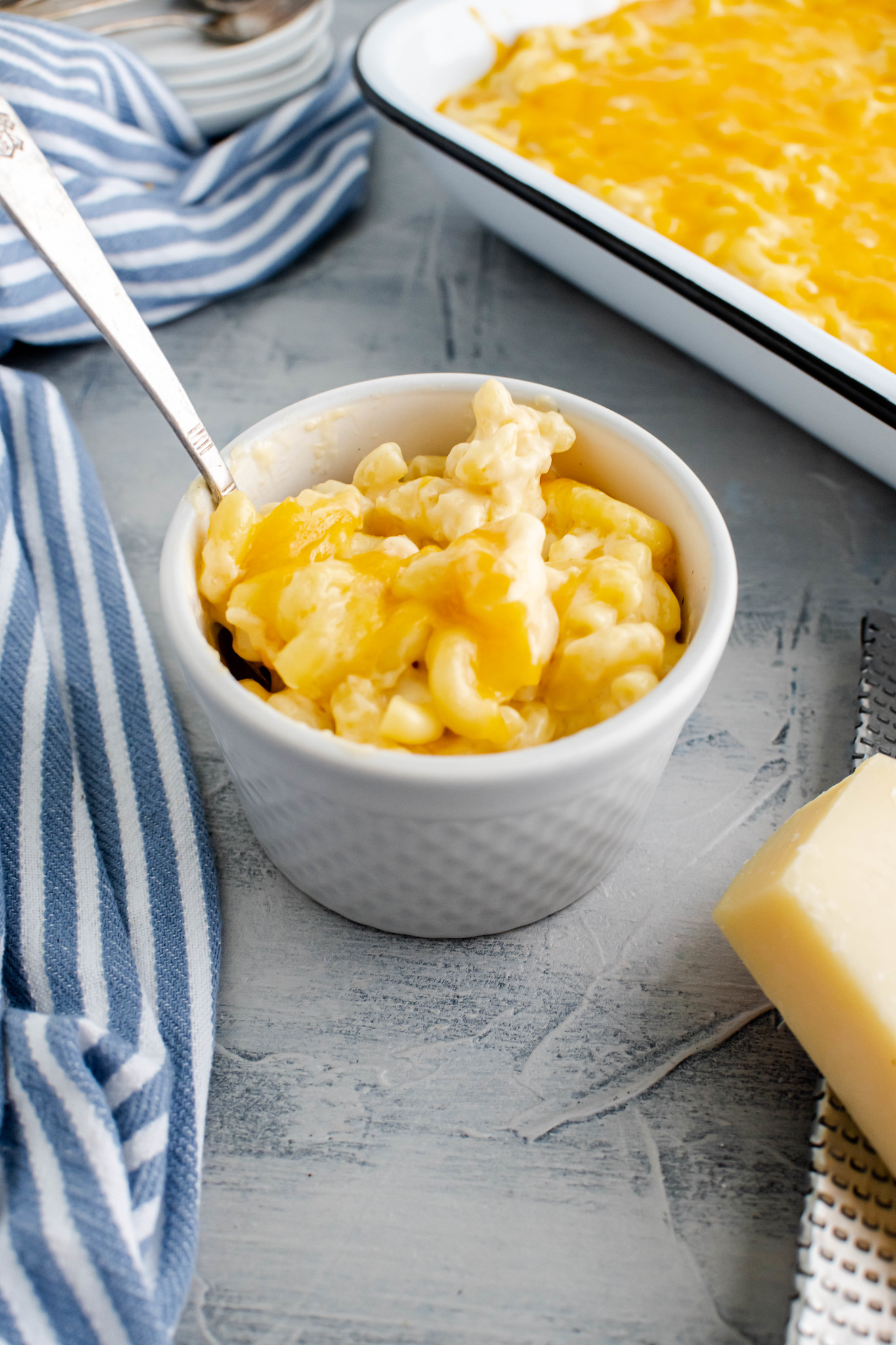 Pale grey bowl filled with macaroni and cheese with a baking dish of macaroni and cheese in the background.