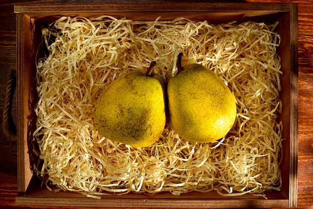 Two ripe pears in a box with shavings on a wooden table, close-up, top view
