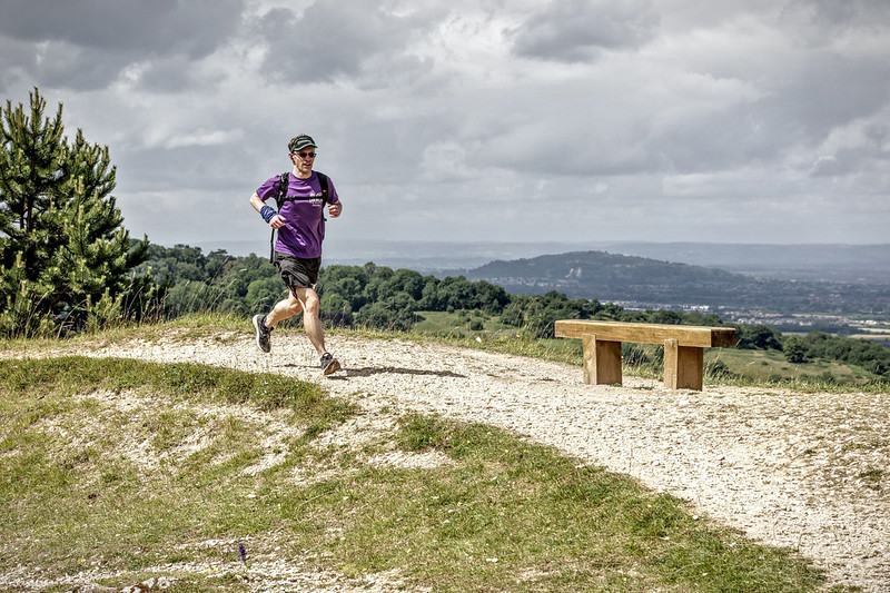 A male runner heading towards a wooden bench with a view behind