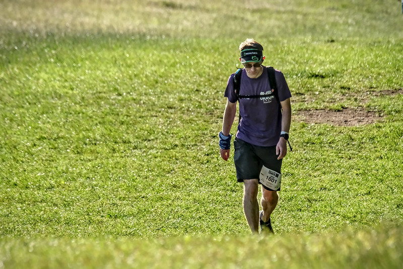 A male runner looking despondetly at the ground as he walks up the hill towards the camera