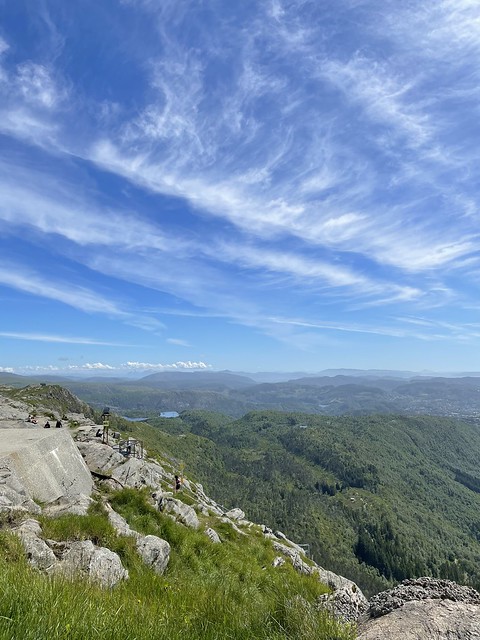 Tree covered mountains spread to the horizon under a blue sky with wispy white clouds.