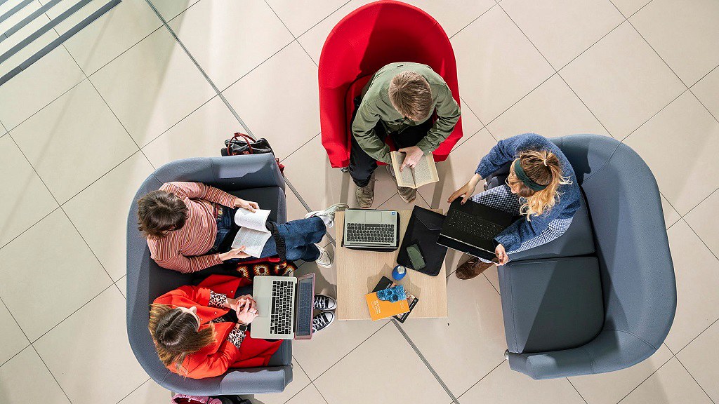 A birds eye view of students sat on sofas with laptops and books
