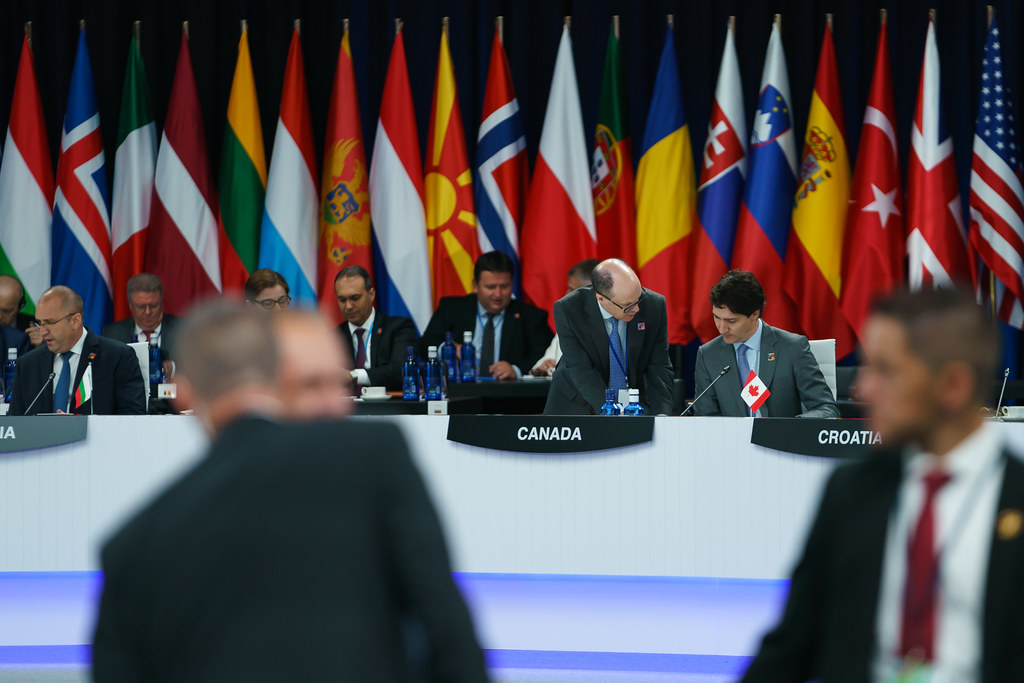Dignitaries sit at a large table, country flags in the background