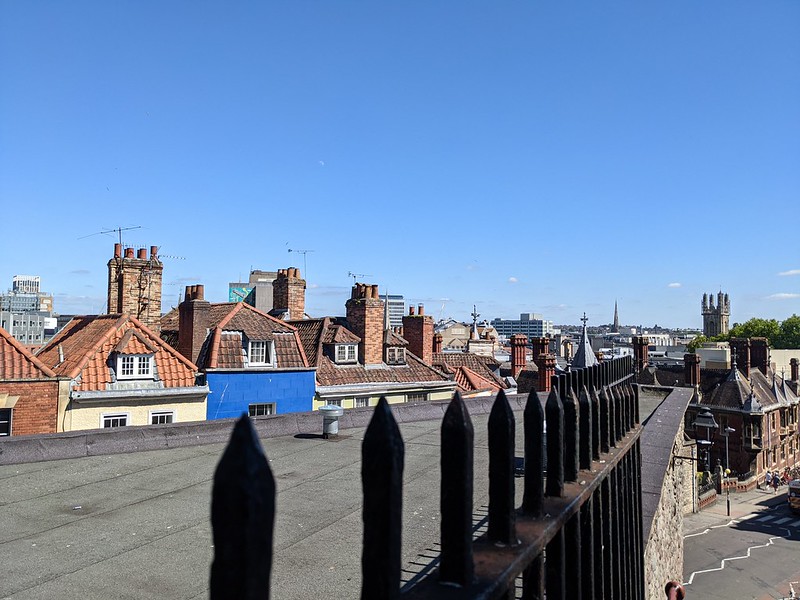 Iron fencing in the foreground, with a church tower in the background and rooftops in between.