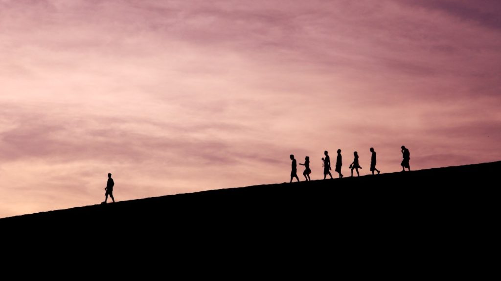 A group of people in silhouette against a sunset, following a leader down a hill
