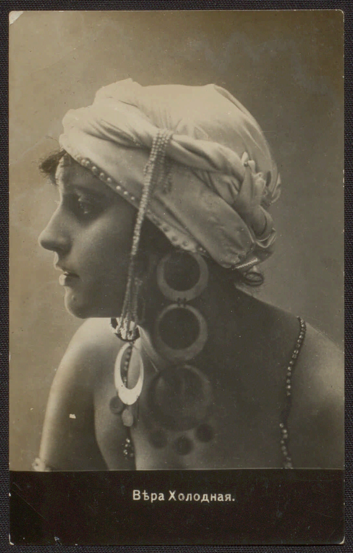 Vera Kholodnaya. Portrait, profile to the left, in a light kerchief tied around the head like a turban, with long earrings consisting of three large circles. Between 1914 and 1919. Postcard from the collection of Natalia Balachenkova. | src Presidential Library