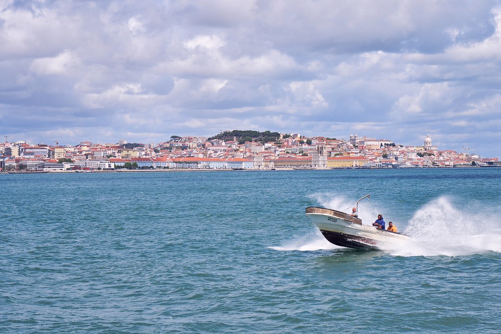 Boat speeding by on the water with lisbon and its mountains in the background