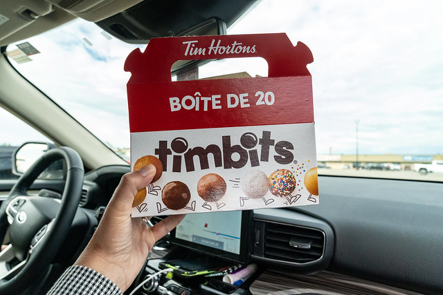 Pincher Creek, Alberta, Canada - July 6, 2022: Hand holds up a box of Tim Horton's Timbits donut holes, while in a car