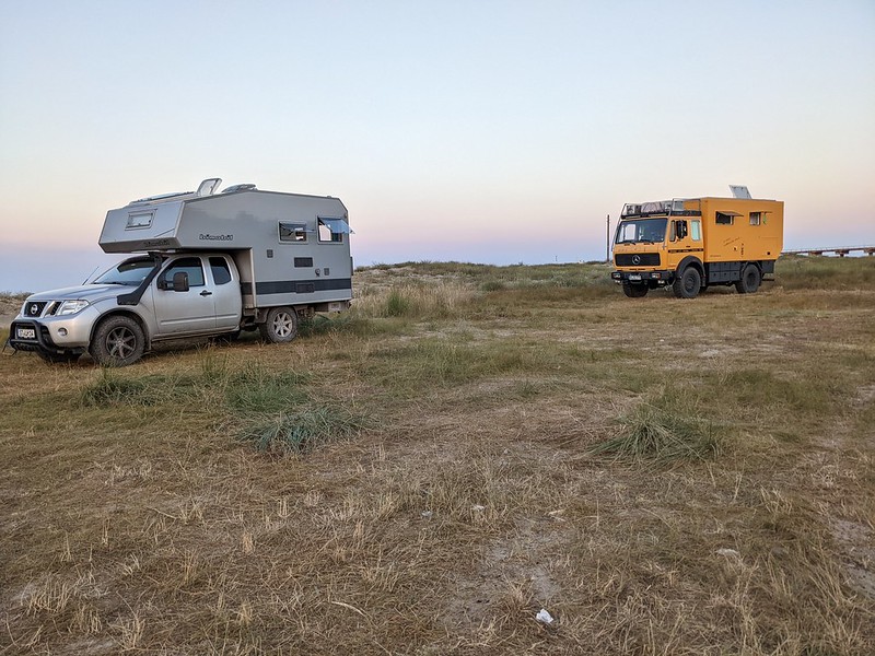 Two campervans, one a grey converted pickup truck and the other a yellow Mercedes lorry, on the beach.