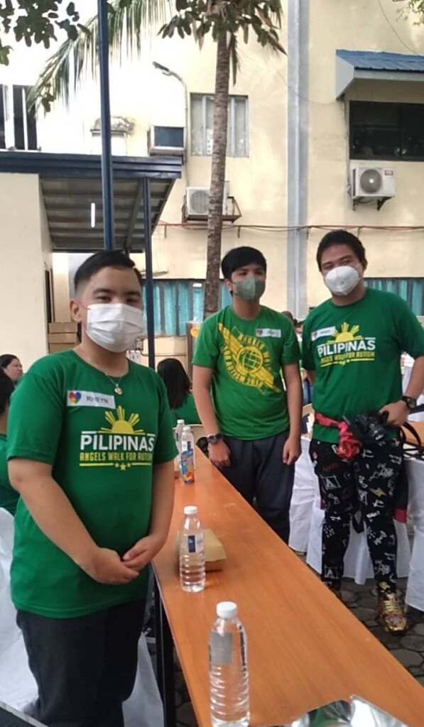PWAs Rhav Lomboy, Zion Cruz and Rheyn Martinez standing in front of a tan thin table with styro of foods, bottles of water and tetra pack of Zesto Juice.