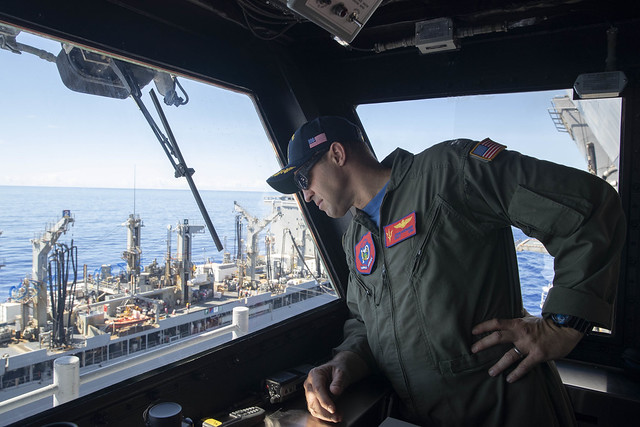 Capt. John Kiefaber, commanding officer of USS Tripoli (LHA 7), observes a replenishment-at-sea from the starboard bridge wing.
