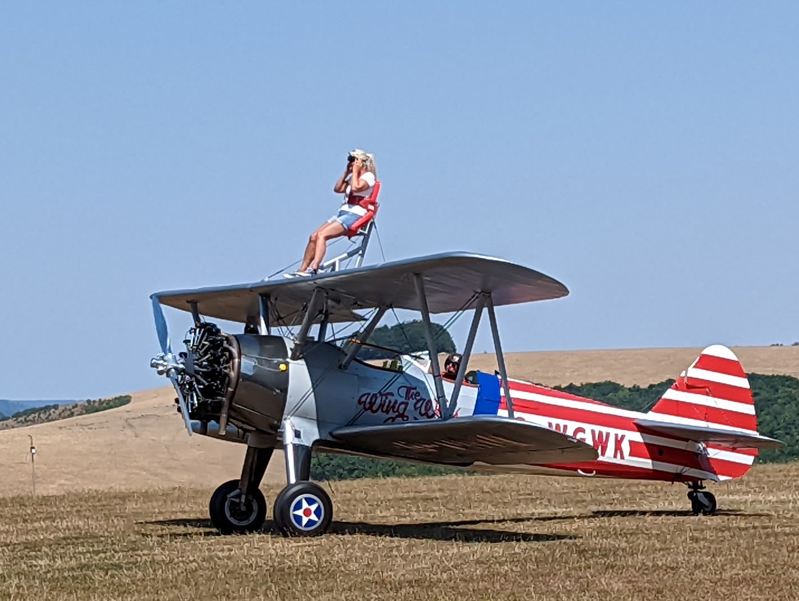 A woman sits strapped to the top of a bi-plane painted in US patriotic decor and about to take off