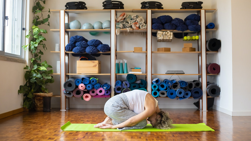 Woman kneels on a yoga mat in front of yoga equipment
