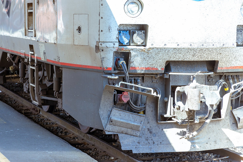 The front of an Amtrak locomotive, showing off covered sockets, the coupler, a thick layer of dirth, and paint starting to peel